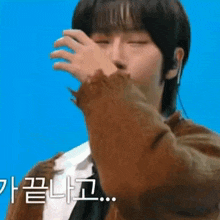 a young man is covering his face with his hand while wearing a brown jacket .
