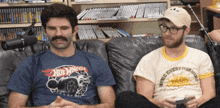 a man wearing a hot wheels shirt sits on a couch