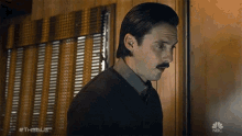 a man with a mustache is standing in front of a window with the hashtag #thisisus