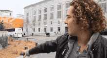 a man with curly hair wearing a black jacket with the letter e on it