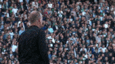 a man in a black shirt is standing in front of a crowd with a few people wearing green shirts