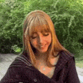 a woman with long blonde hair and bangs is wearing a black sweater and a necklace .