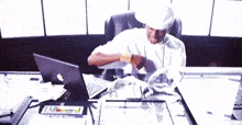 a man sitting at a desk with an apple laptop and a billboard sign