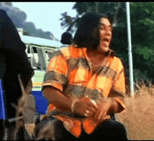 a man wearing a plaid shirt is sitting in a field with his mouth open