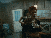 a woman with red hair is standing in a room with the words terasgifs on the bottom right corner