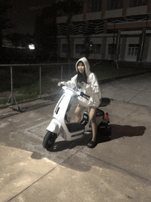 a girl in a white hoodie sits on a white scooter with a license plate that says lg