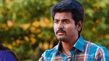 a man with a mustache is wearing a blue and red plaid shirt .