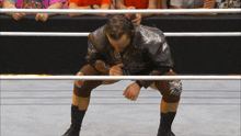 a wrestler kneeling down in a ring with a crowd behind him