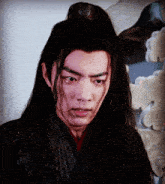 a man with long hair and a ponytail looks at the camera with a serious look on his face