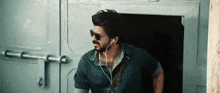 a man wearing sunglasses and ear buds is standing in front of a door .