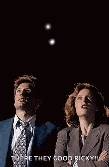 a man and a woman are looking up at a flying object in the dark .