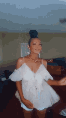 a woman in a white dress is standing in a living room and smiling .