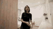 a woman in a black shirt is standing next to a bed in a bedroom