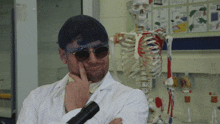 a man in a lab coat holds a microscope in front of a skeleton model