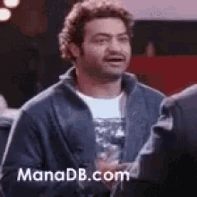 a man in a blue jacket is making a funny face while standing in front of a group of people .