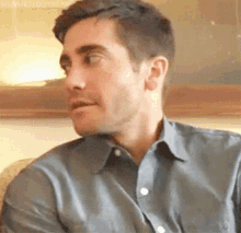 a man in a grey shirt is sitting on a couch and making a funny face