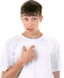 a young man in a white t-shirt is pointing at his chest .
