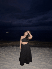 a woman in a black dress stands on a sandy beach at night