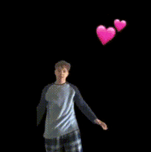 a man is standing in front of two pink hearts flying in the air