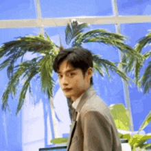 a man in a suit and tie is standing in front of a palm tree .
