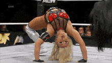 a woman is doing a handstand in a wrestling ring while a man watches .