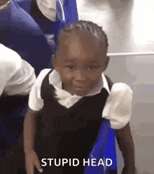 a little girl in a school uniform is sitting on a chair and smiling .