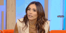 a woman is sitting on a couch wearing a gold necklace and a white vest .