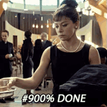 a woman in a black dress with a pearl necklace is holding a tray of food and says # 900 % done