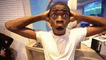 a man in a white shirt has his mouth open and his hands on his ears