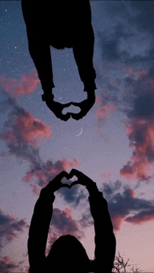 two people are making a heart shape with their hands against a cloudy sky