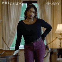 a woman in a black shirt and purple jeans is standing in front of a window with wildcards written on the bottom