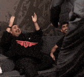 three men are sitting on a couch and one of them has the word viva written on the wall behind them