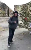 a young man standing next to a christmas tree giving the thumbs up sign