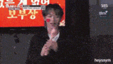 a man with a red heart painted on his face is holding a microphone in front of a red sign .