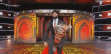 a man in a suit and tie is holding a wwe championship belt .