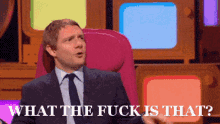 a man in a suit and tie is sitting in front of a screen that says what the fuck is that