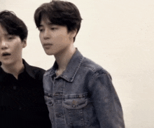 two men are standing next to each other and one of them is wearing a denim jacket .