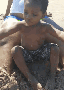 a little boy is sitting on a pile of sand on the beach