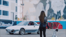 a woman is walking towards a white car with a license plate that says eaa nsd