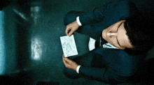 a man in a suit is sitting on the floor holding a piece of paper