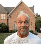 a man with a beard is standing in front of a brick house and says `` ill kill you '' .