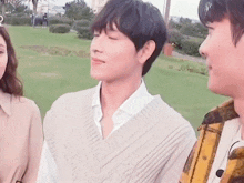 a man wearing a sweater vest is standing in a park with other people .