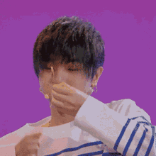 a young man wearing a striped shirt is making a heart shape with his hands against a purple background .