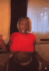 a woman in a red shirt with a pacifier in her mouth is sitting in front of a window .