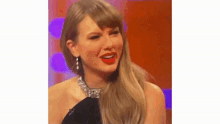taylor swift is wearing a black dress and a necklace and smiling while sitting on a stage .