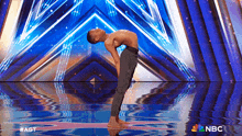 a shirtless man is doing a yoga pose on a stage with a nbc logo behind him