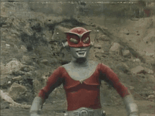 a man in a red costume is standing in the dirt with his arms crossed ..