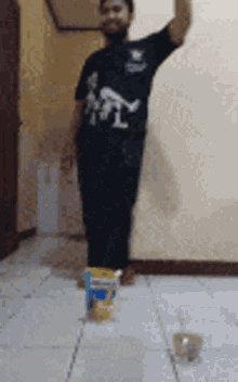 a man in a black shirt is standing on a tiled floor with a bag of chips on the floor .