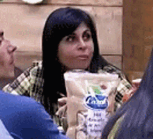a woman with long black hair is sitting at a table holding a bag of food .