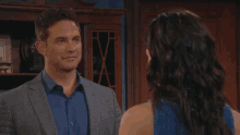a man in a suit stands next to a woman in a blue shirt